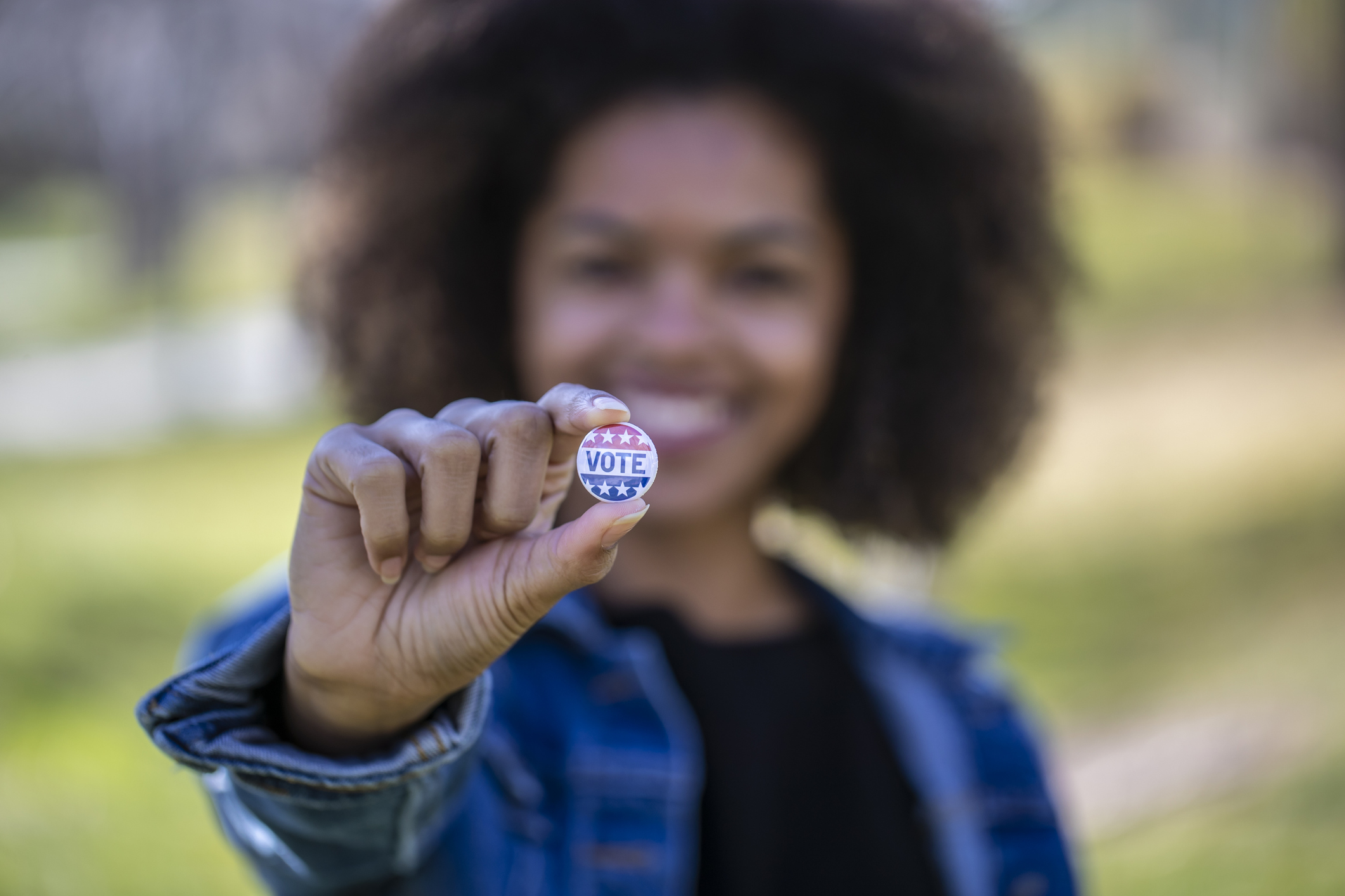 A young African American woman holding a voting badge.