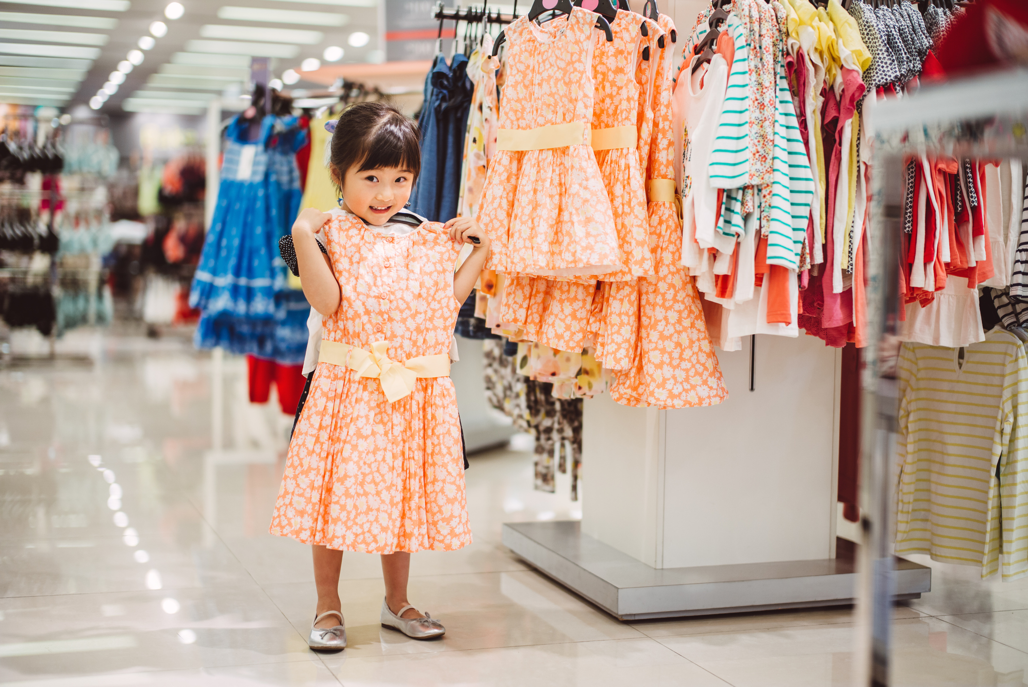 Lovely little girl trying out new dress at department store while looking in the camera joyfully