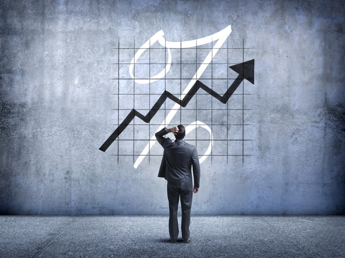 A businessman places his hand on his head as he is perplexed by a chart indicating rising interest rates.